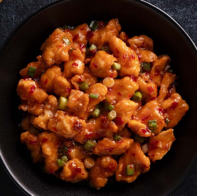 bowl of orange chicken with green onions and chili flakes