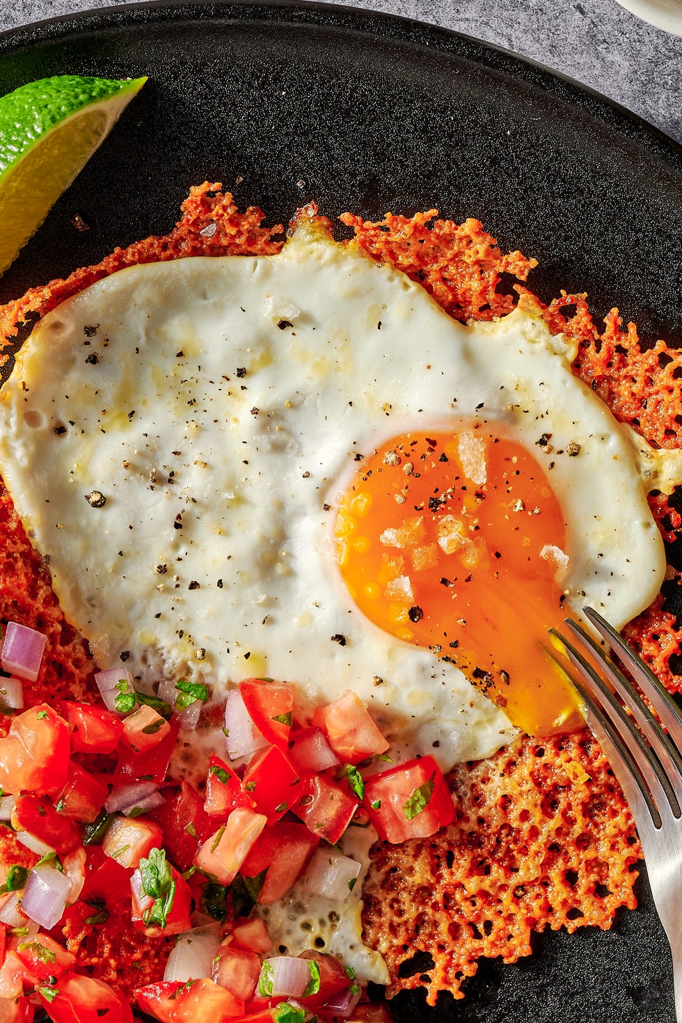cheesy frico fried egg tostadas on a black plate with pico de gallo