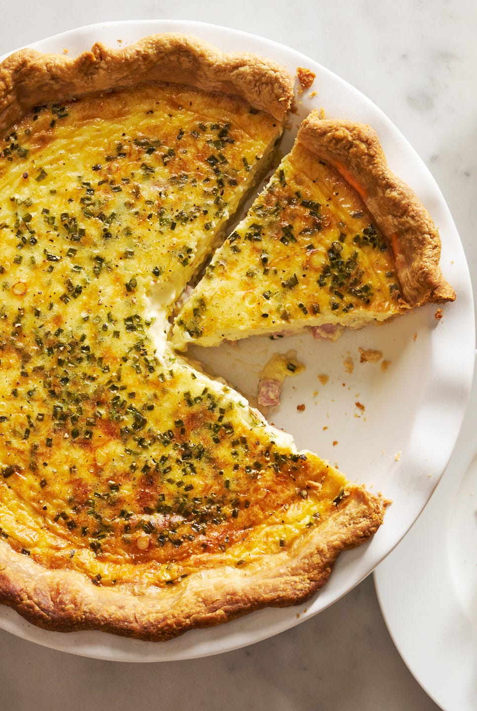 ham and cheese quiche beside a plate with a slice of quiche and a salad bowl