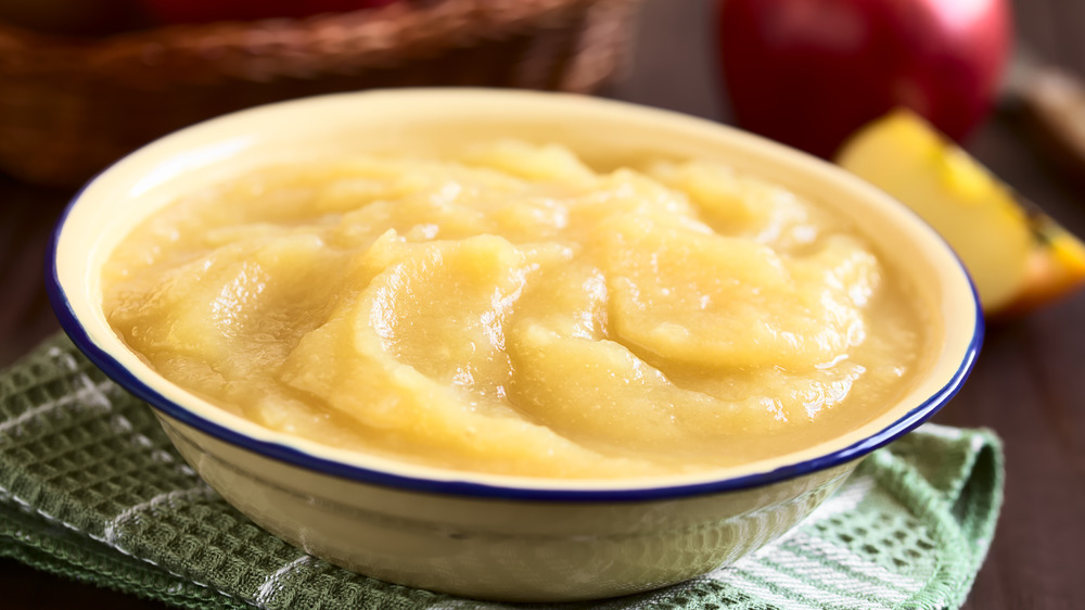 A bowl of applesauce on a green napkin with apples in the background.