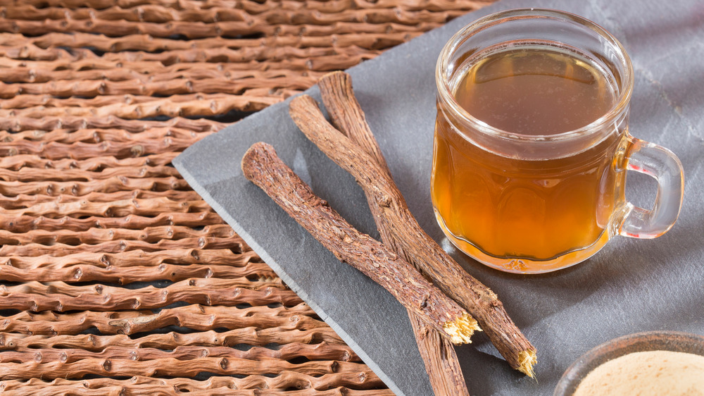 A glass of licorice tea next to licorice roots and powder on a gray plate.