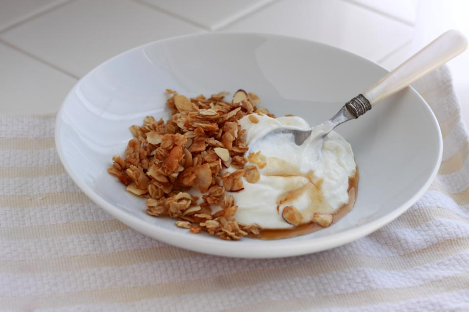 A bowl of greek yogurt with homemade granola and a drizzle of agave nectar, on a striped dishtowel in the kitchen
