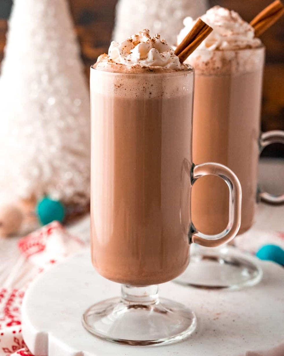 eggnog hot chocolate in glass mug with whipped cream and cinnamon stick