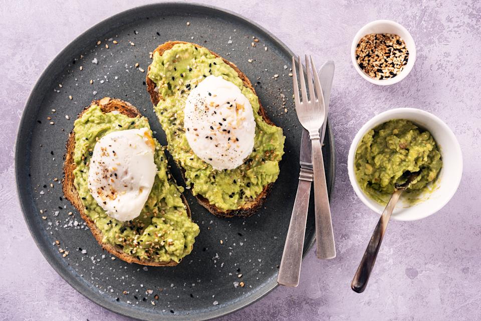 Overhead view of 2 slices toasted crusty bread with a thick layer of mashed avocado that has been seasoned with some salt and pepper and lemon juice, with a two poached organic eggs on top with some toasted sesame seeds sprinkled on top. Perfect for lunch or a light dinner. Colour, horizontal format with some copy space.