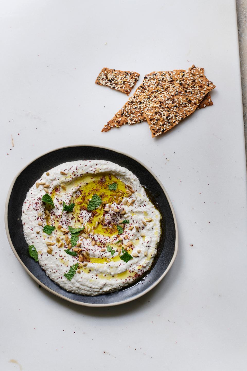 A plate smeared with a white dip and sesame crackers.