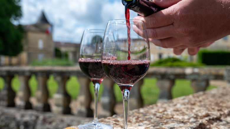 An individual pouring red wine into glasses in Bordeaux, France.