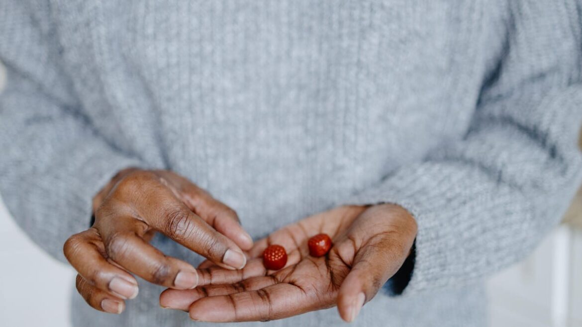 A close up of a person's hand holding two red gummy supplements. They are wearing a light grey sweater.