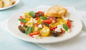 Summer heirloom tomato salad with fresh feta cheese on white plate on blue background, selective focus, horizontal