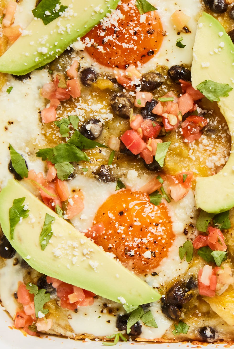 huevos rancheros casserole in a baking dish with topped with sliced avocado, cilantro, and sour cream