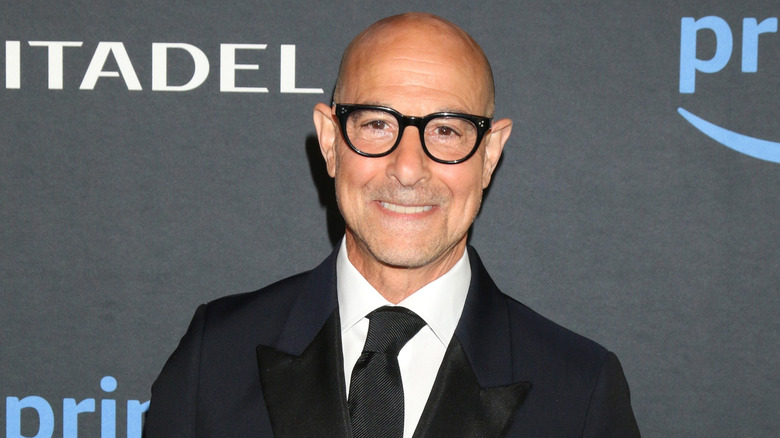 Stanley Tucci wearing glasses and a black suit at an event.