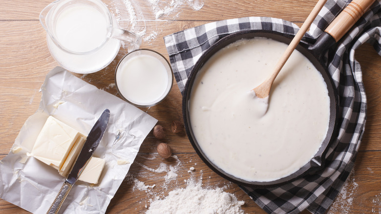 Béchamel sauce in a pan, with the ingredients for it dotted around it