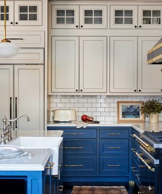 Bistro style kitchen with white subway tiles, blue cupboards with gold handles, vintage pendant light and white cabinets