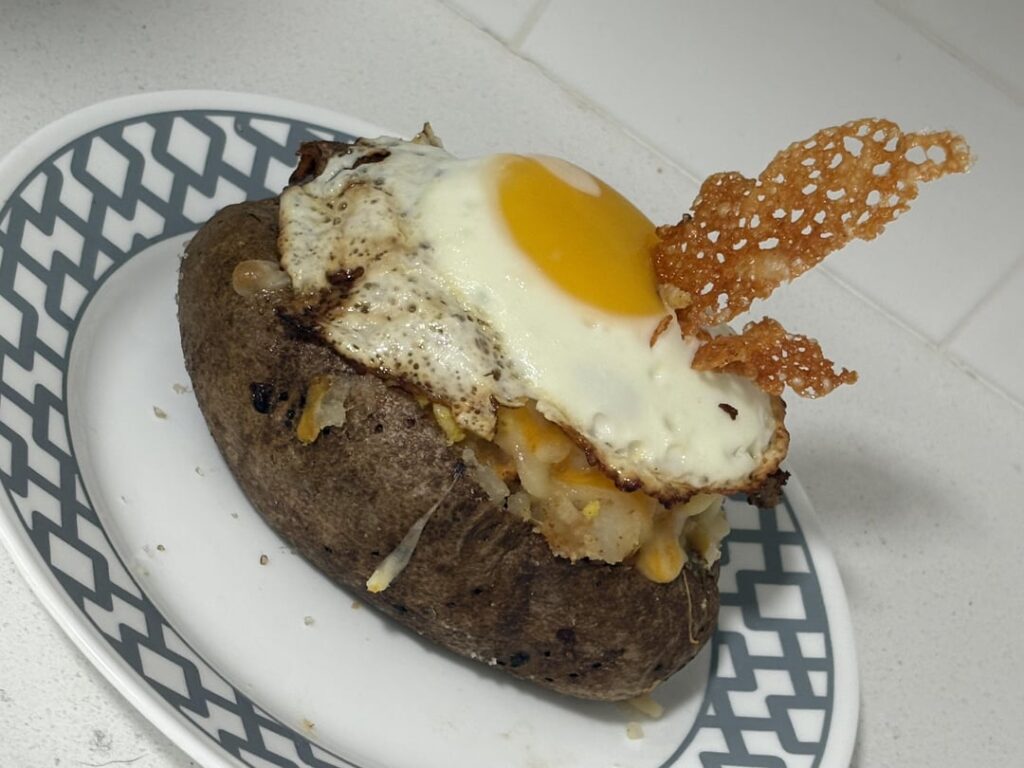 Twice baked potato with sunny side egg and left over cheese on the pan