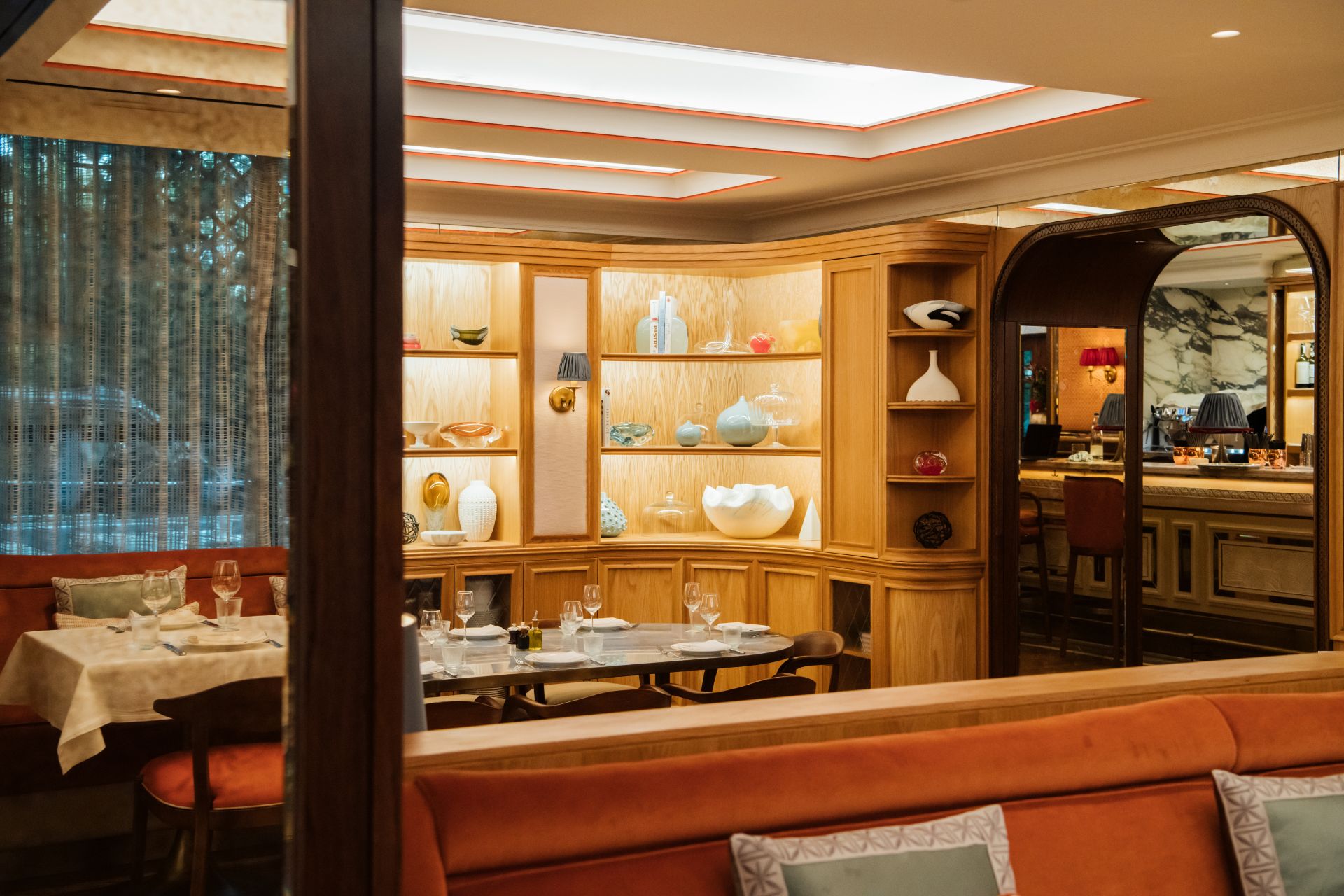 Rstaurant with rose pink banquettes, pale ok shelves and white marble-topped tables