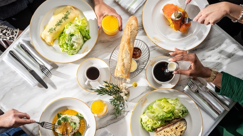 The hands of four women eating brunch plates at Chez Maggy