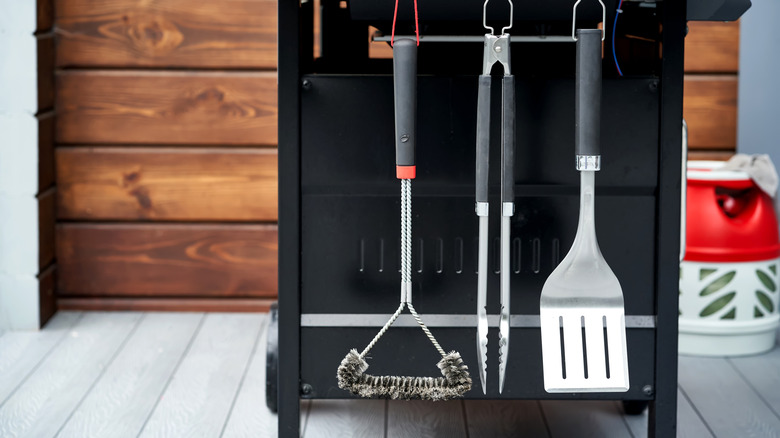 A gas grill with cooking utensils hung on the side