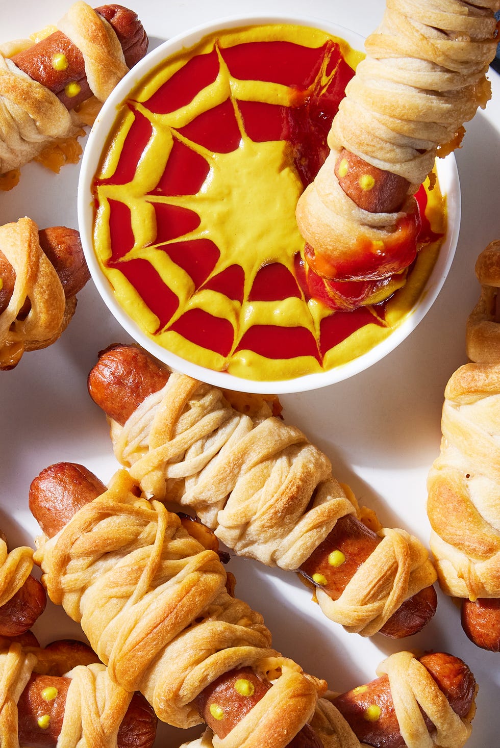 hot dogs with mustard eyes wrapped in crescent dough with cheese and served a mustard and ketchup dip