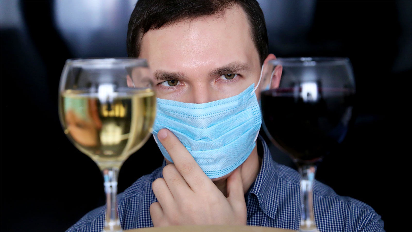  A man in a mask considers two glasses of wine.