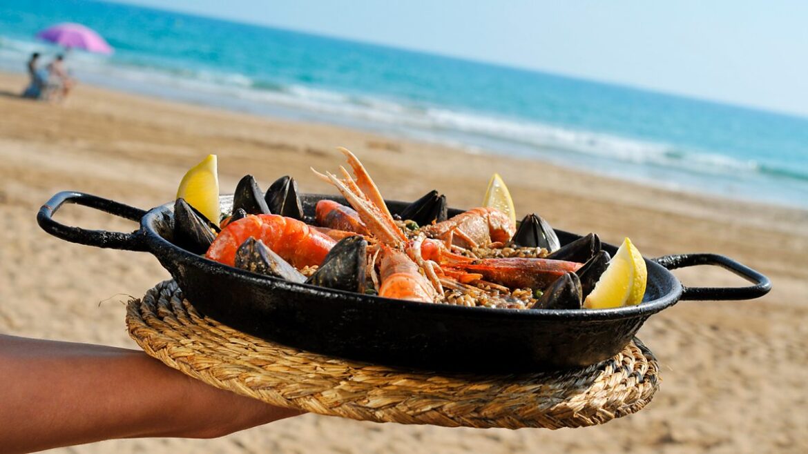 Paella in a pan with the beach and sea in the background