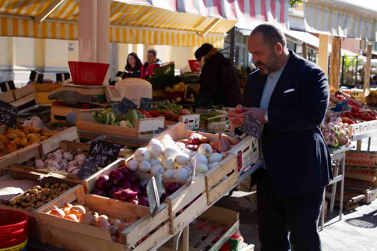 A man stands in front of a market stall looking at produce.