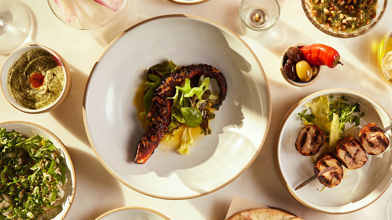 Grilled octopus on a plate next to a salad, pita and other dishes at Iris Restaurant