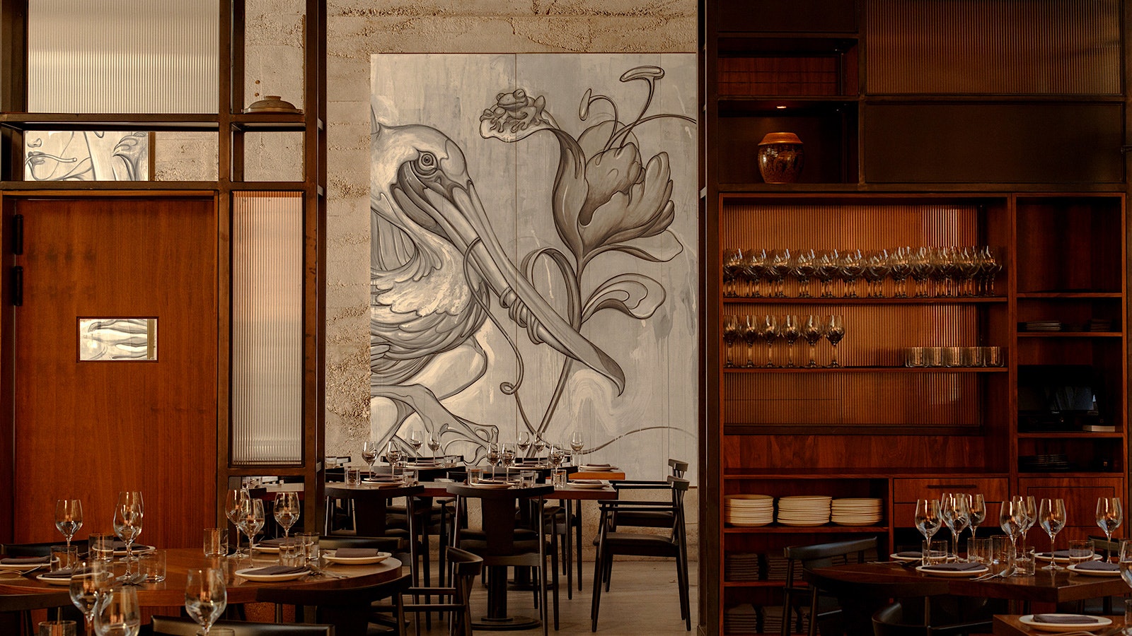 A hung painting of a pelican near tables set with wineglasses at Majordomo