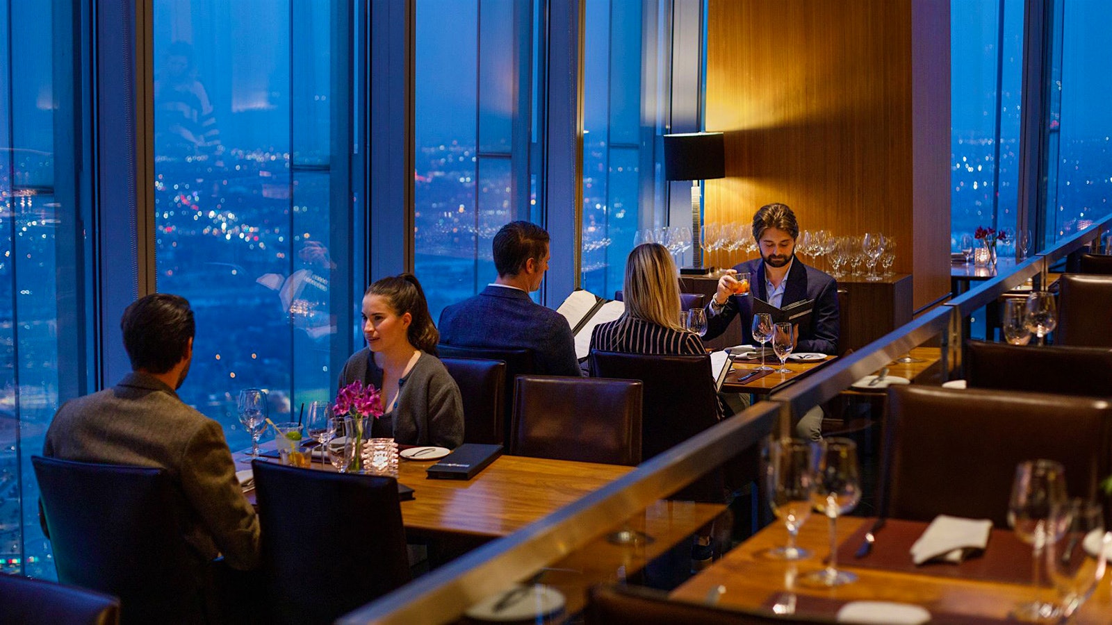 People dining on leather chairs at wood tables near a table of wineglasses at Vast, with a view overlooking Oklahoma City