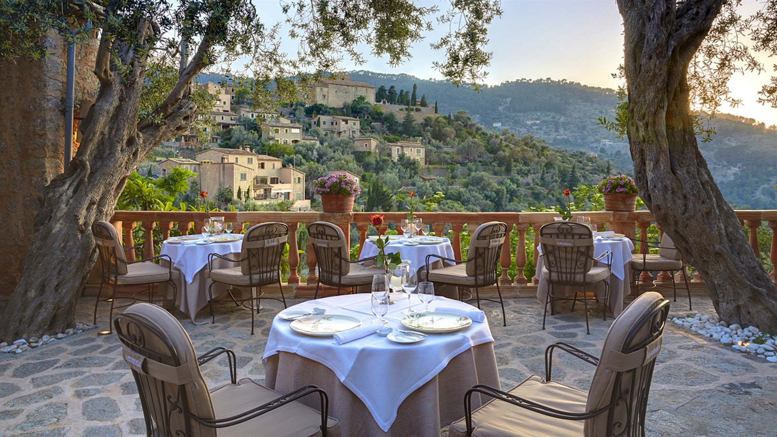  A set table on a veranda at El Olivo, with a view of hills and old stone buildings on a hillside