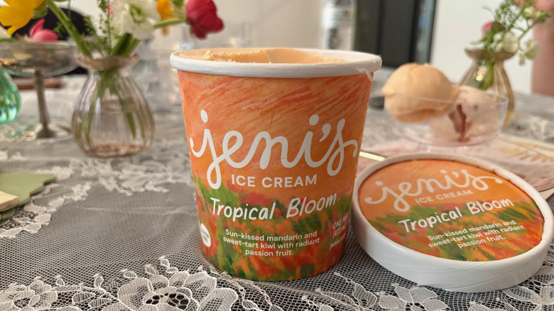 Open pint of Jeni's Tropical Bloom ice cream with a dish of two scoops on the table behind it