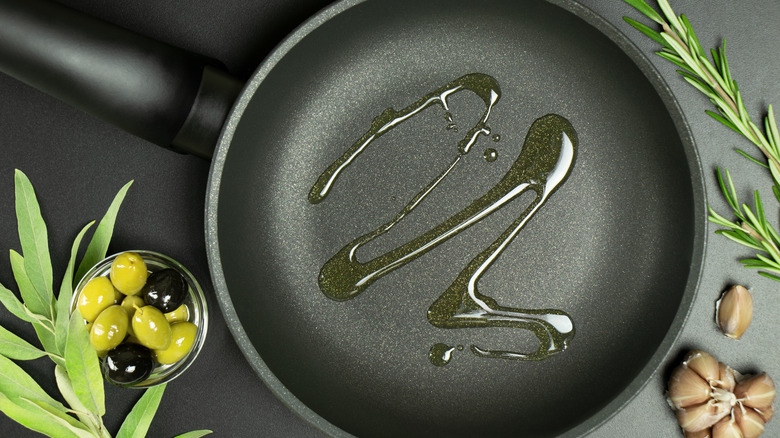 top view of a frying pan with olive oil drizzled inside next to garlic and olives
