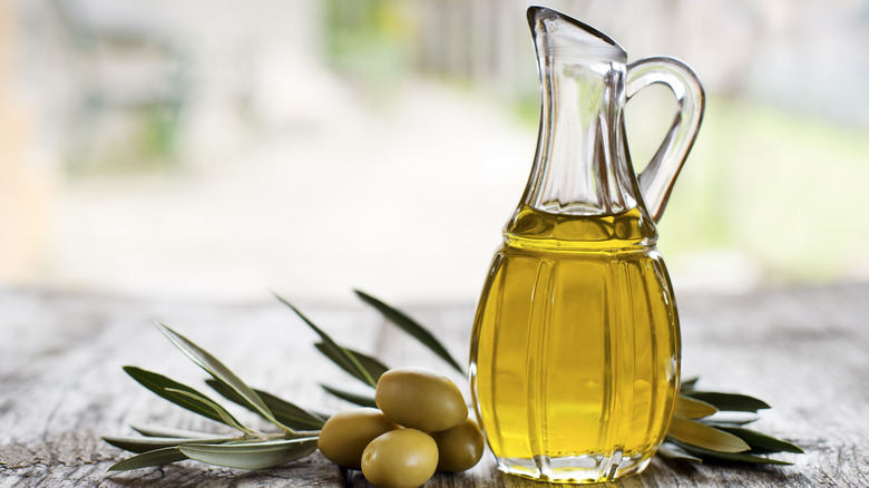 a glass bottle with light olive oil next to a small branch with olives