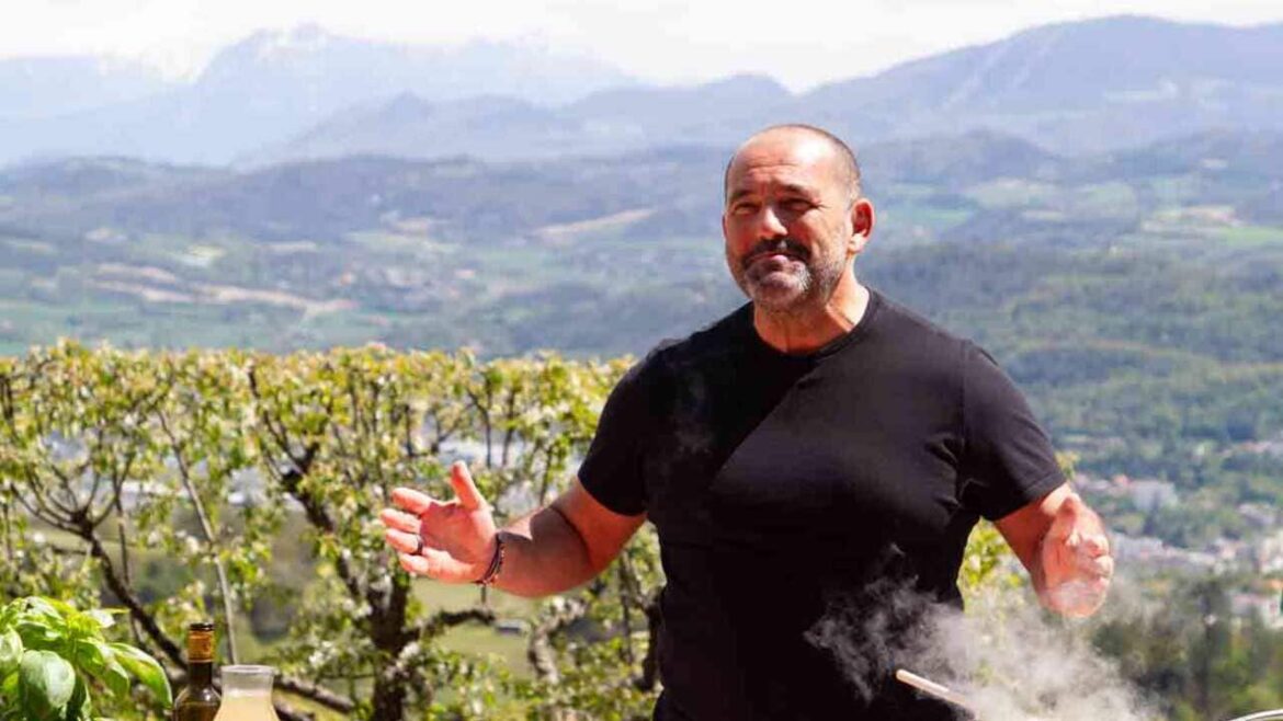 Plat du Tour S5 | Episode guide A man in a black t-shirt stands in a vineyard, with a saucepan on a portable stove on the table in front of him. Rolling mountain scenery can be seen behind him.