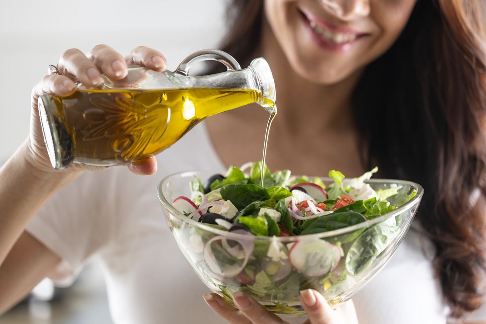 Woman pouring olive oil into salad