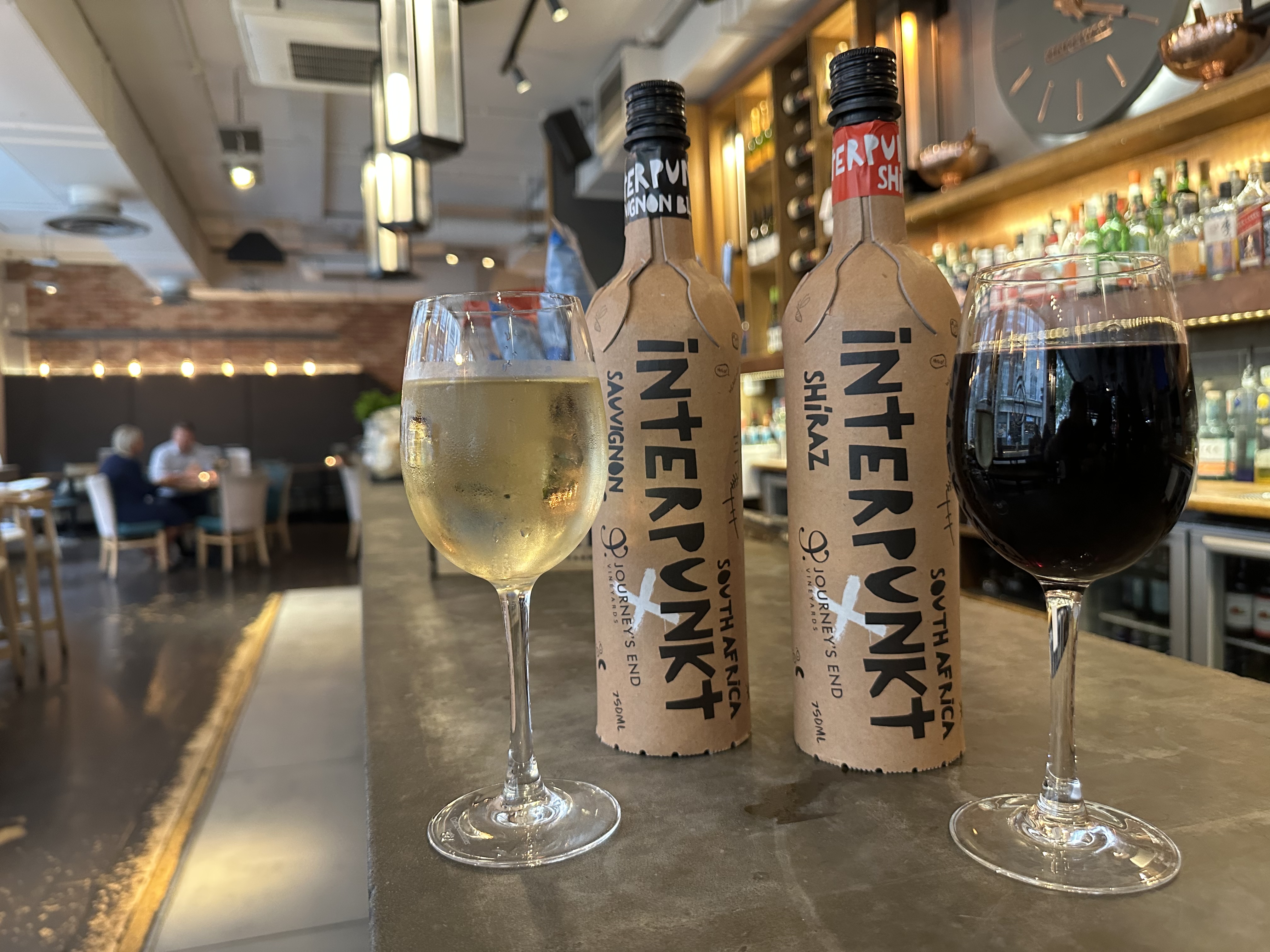 Two glasses of wine, one white and one red, next to their respective bottles.