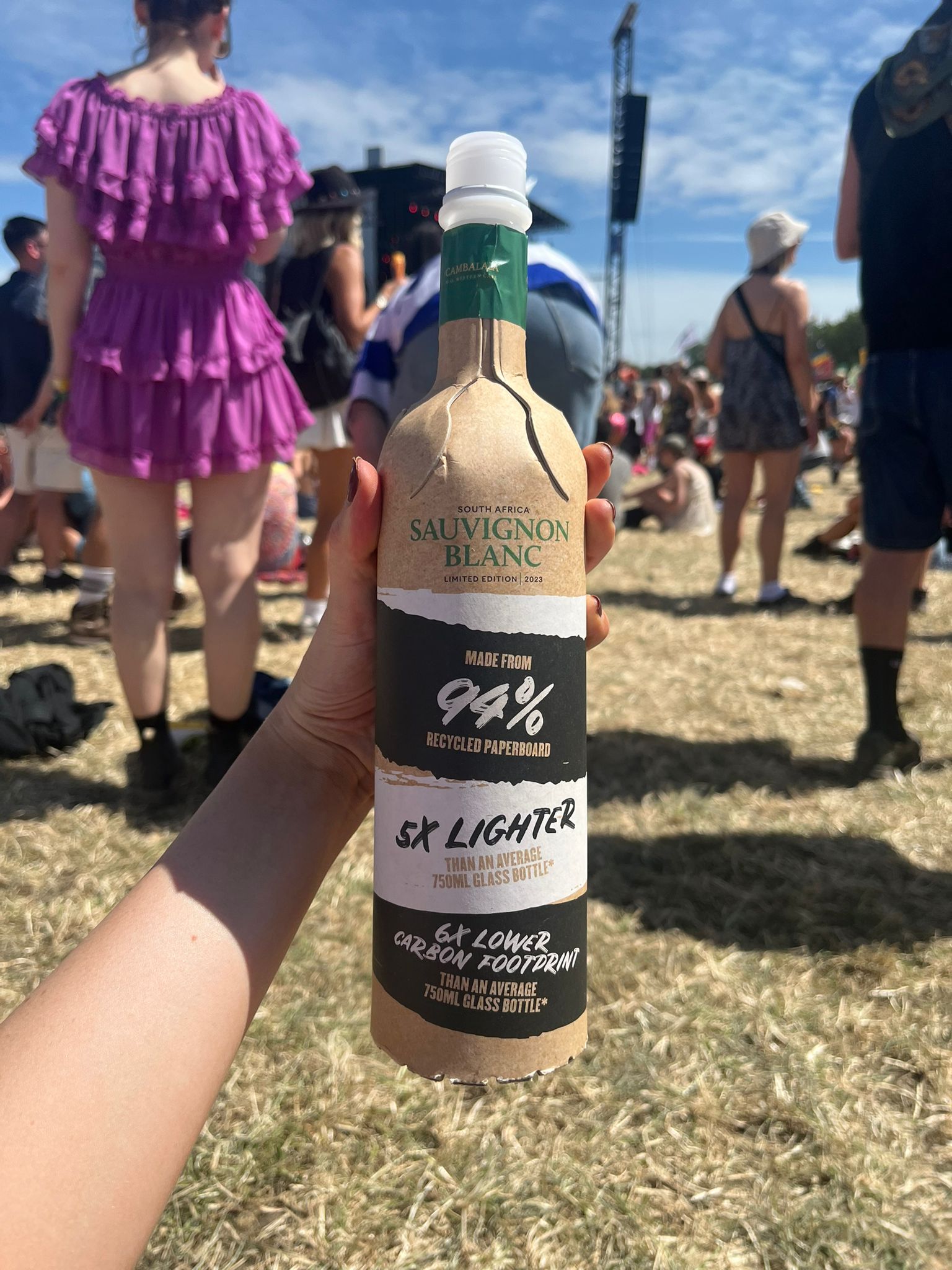 A hand holding a cardboard bottle of Sauvignon Blanc at an outdoor event.