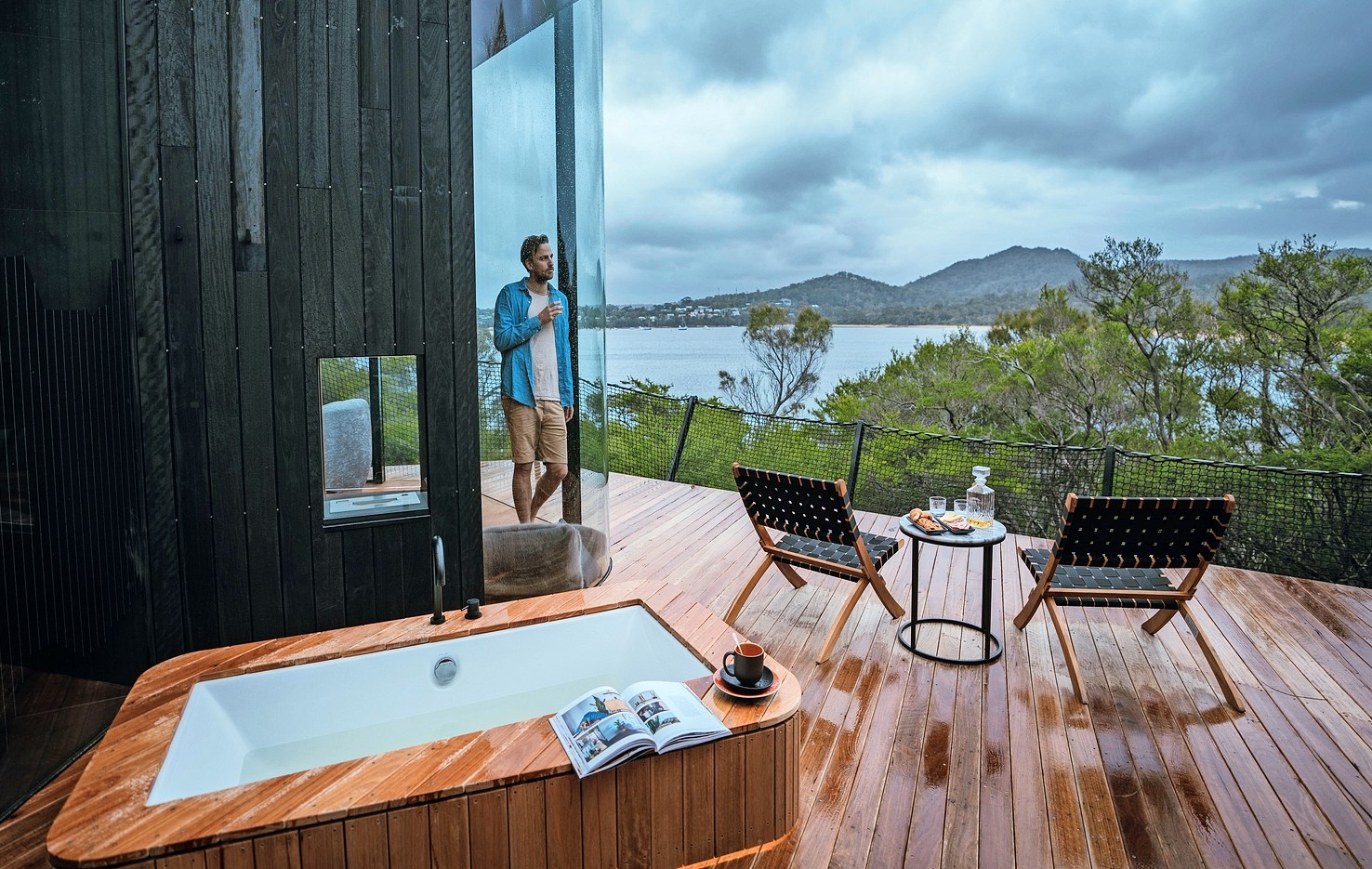 Man enjoying a drink on a deck overlooking a bay.