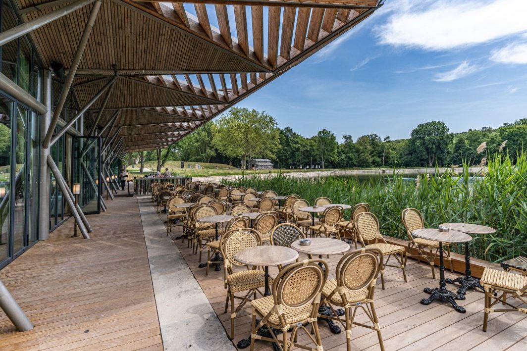 Outdoor restaurant patio with wicker chairs and tables overlooking a pond.