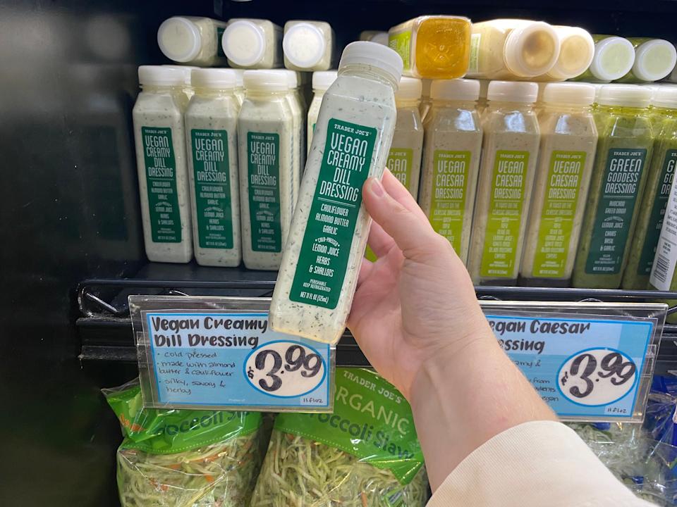 hand holding bottle of vegan dill dressing in front of a fridge of dressings at trader joes