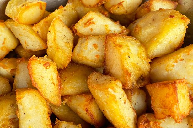 Stock photo showing an elevated view of the inside of a metal bowl with a pile of golden, freshly cooked roast potatoes.