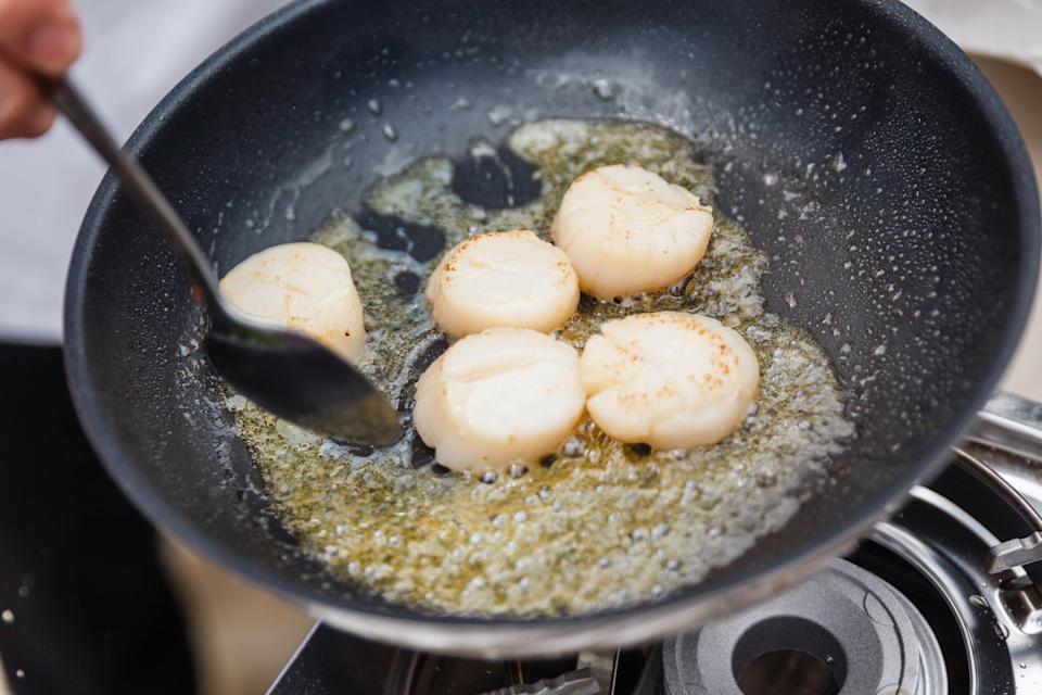 Scallops searing in a frying pan with butter, being turned by a spatula