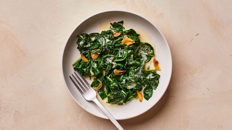 Sauted spinach with sliced garlic and creme fraiche in a shallow bowl with a fork