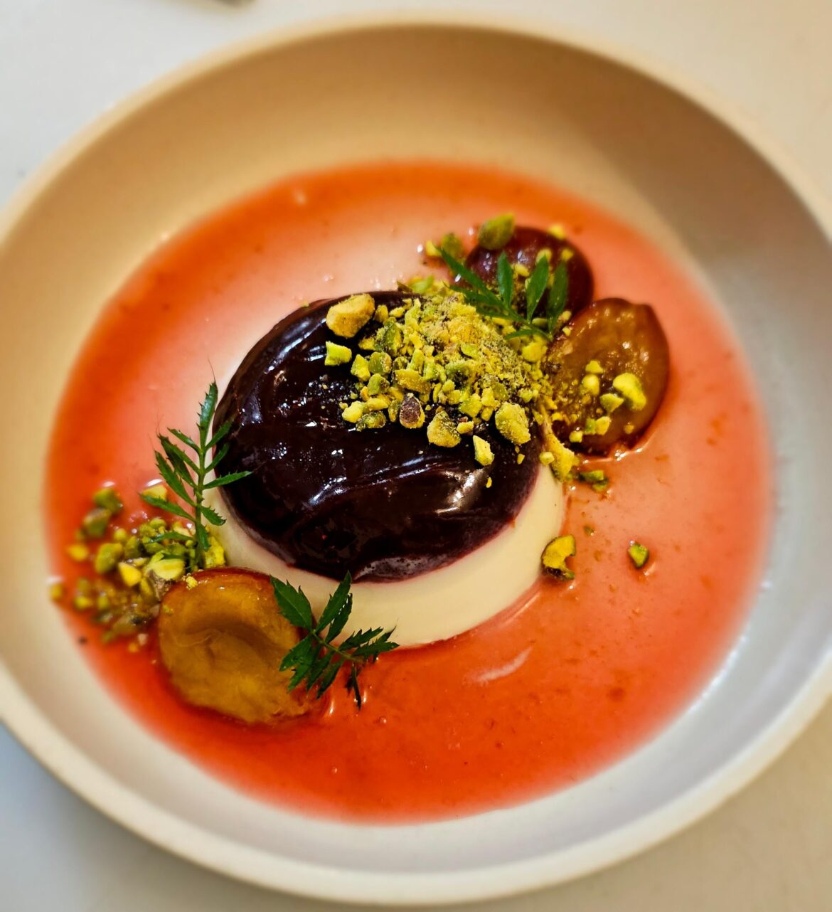 Rose water and plum gel panna cotta, pistachio, marigold leaf, confit plums and plum syrup.