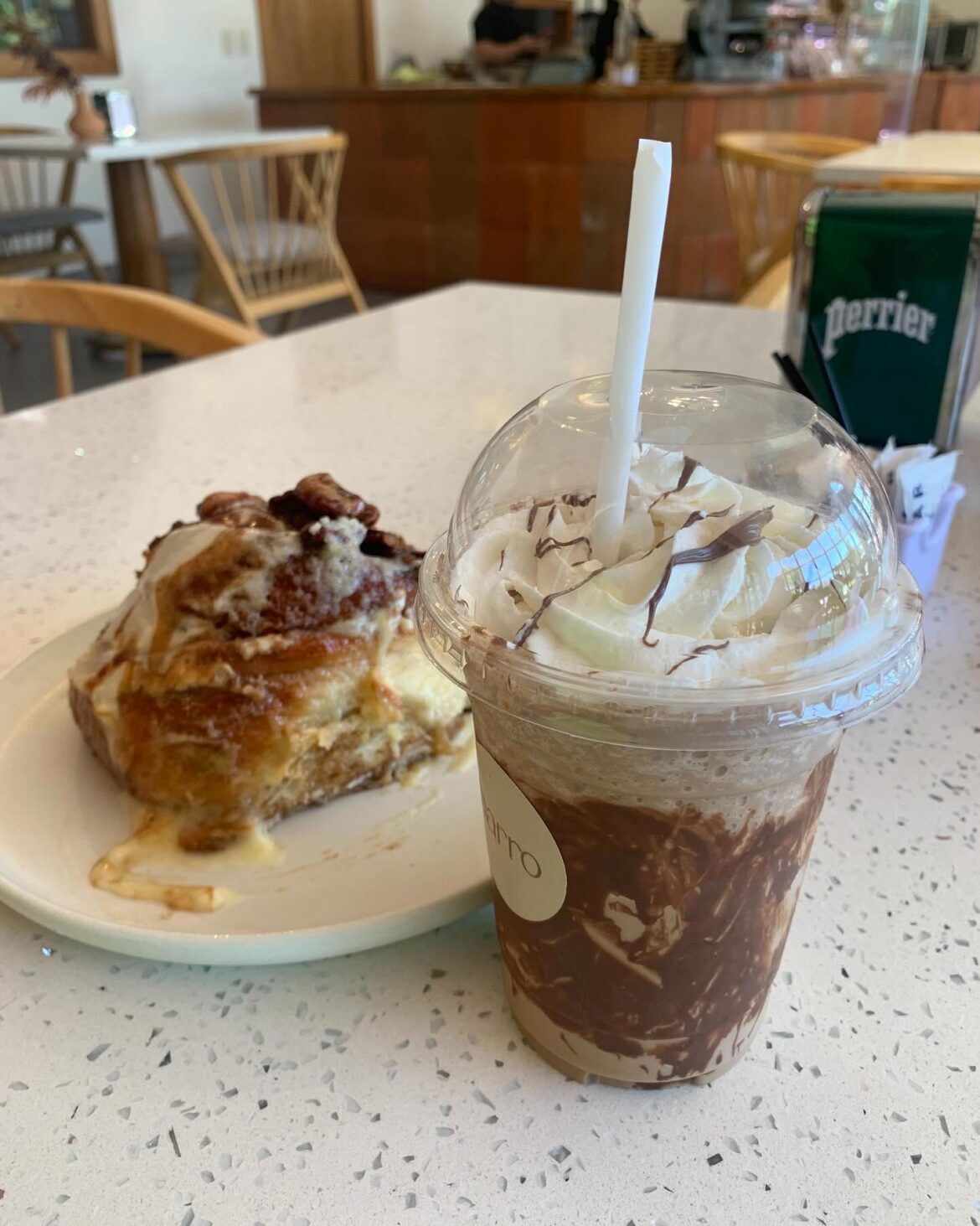 A coffee frappe with a glazed cinnamon roll topped with nuts.