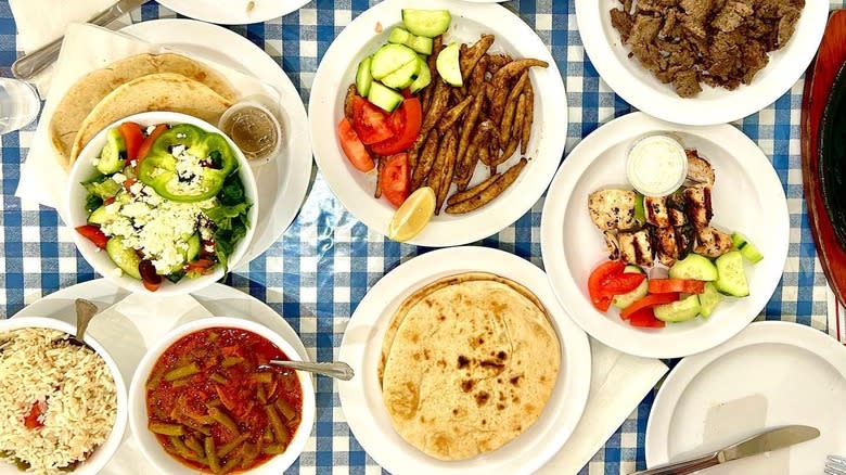 Multiple plates of Greek food on blue checkered tablecloth