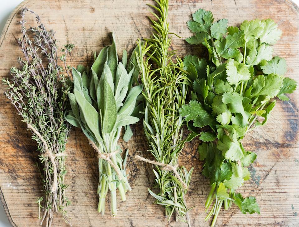 Bundles of fresh herbs tied with twine on a wooden surface: thyme, sage, rosemary, and cilantro