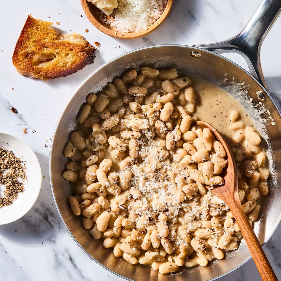 cacio e pepe white beans skillet with a wooden spoon beside a bowl of cheese