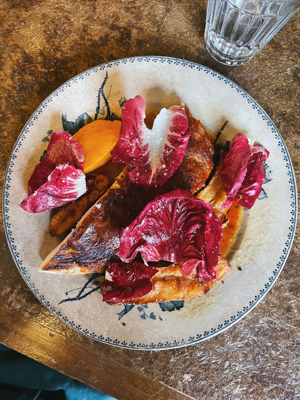 A closeup on a skin-on chicken breast with bright purple radicchio leaves.