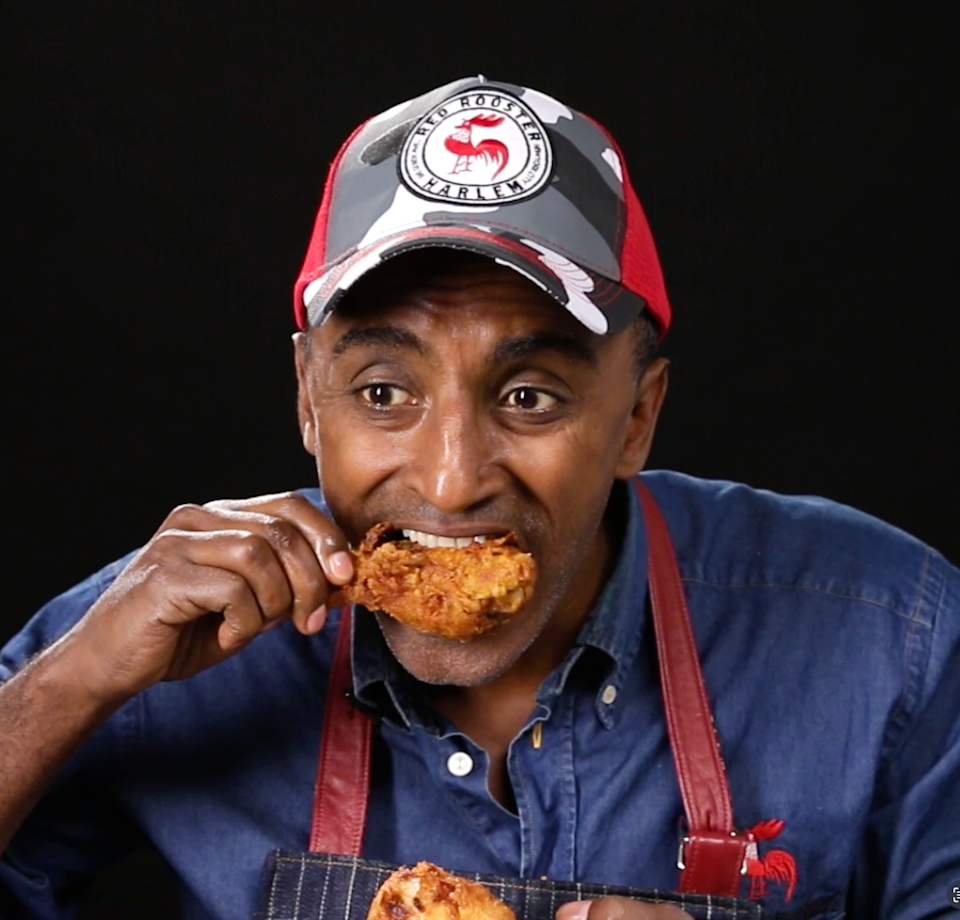 A person wearing a cap and denim shirt with apron bites into a fried chicken drumstick