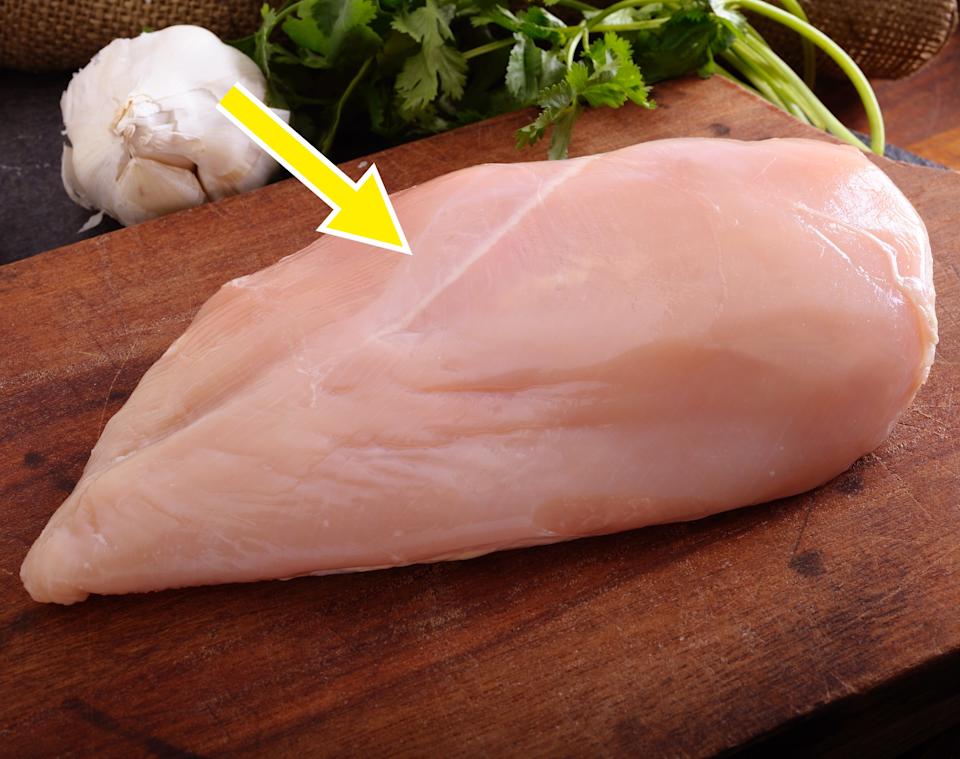 Raw chicken breast on a wooden cutting board with garlic and cilantro in the background