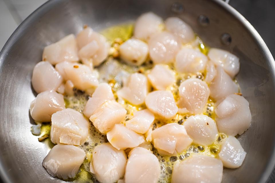 Scallops being seared in a pan with butter